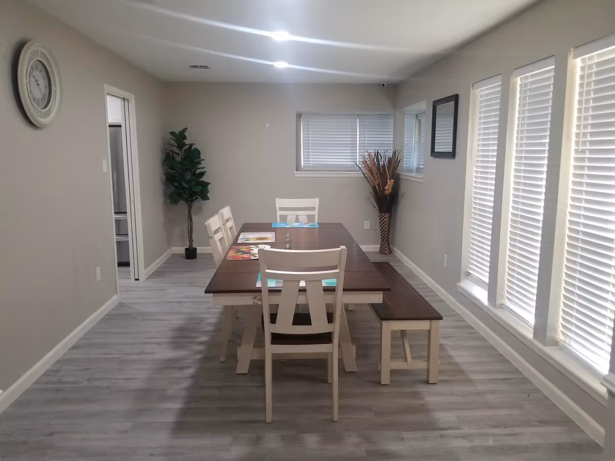 Dining room with a wooden table, bench and chairs centered in a bright room with large windows and blinds.