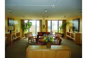 Bright senior living lounge with plants, comfortable seating, and large windows.