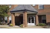 Front entrance of a brick senior living facility with pillars and glass doors.