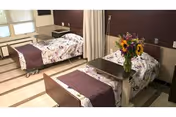 Two hospital beds with purple floral bedding and a shared curtain in a double-occupancy patient room.
