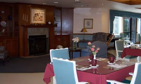 A senior living dining room with tables set for meals and a fireplace.