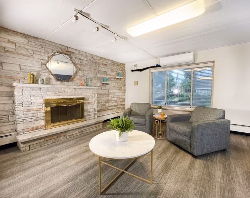 Cozy seating area with two gray armchairs, a round marble-top coffee table, and a stone fireplace along one wall.
