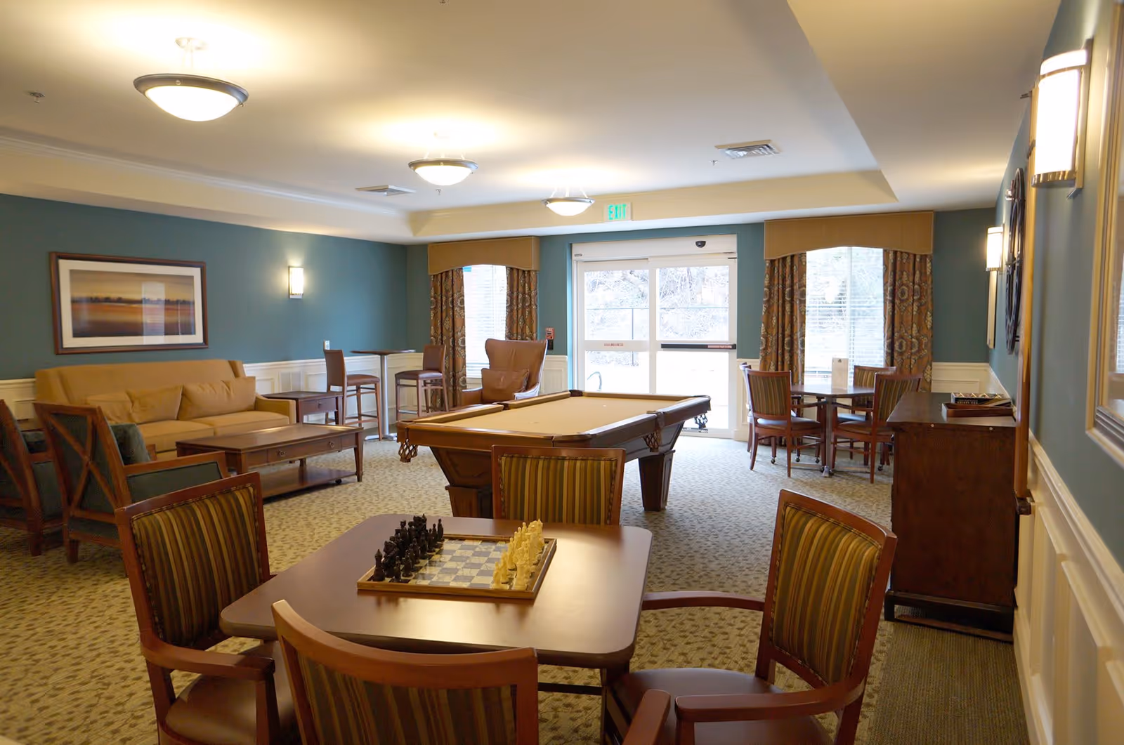 A bright communal lounge with a pool table, chessboard on a table, seating areas and large windows.