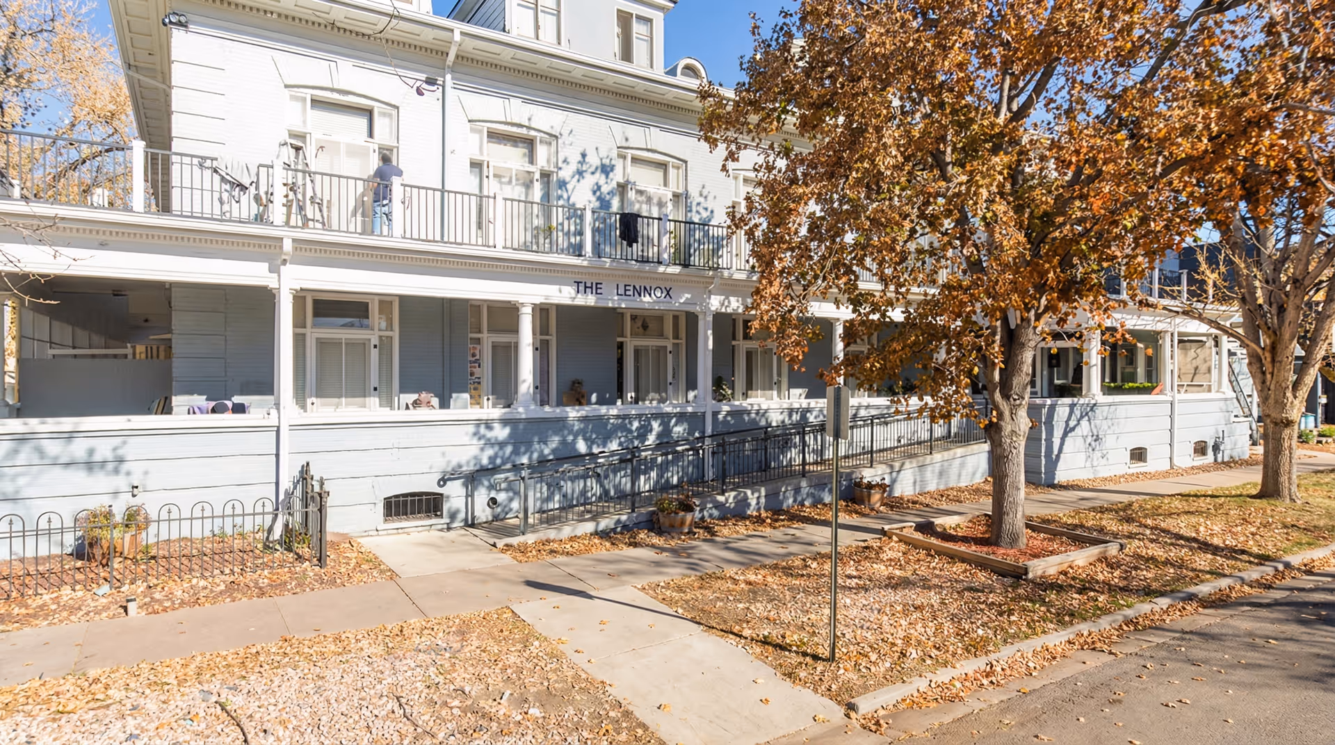 Exterior view of Lennox Guest Home with a wraparound porch and autumn trees.