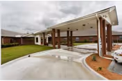 Covered drive-through entrance (porte-cochère) of a single-story brick care facility with a wet concrete driveway and columns.