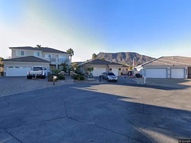 A cul-de-sac with several single-family homes and parked vehicles, set against a backdrop of a mountain under a clear blue sky.