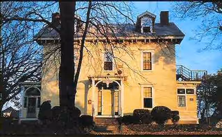 Yellow two-story house-style building with arched entrance and surrounding shrubs