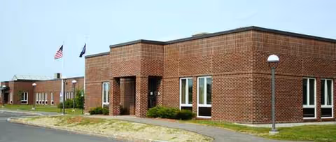 Brick building exterior of a senior living facility with flagpoles and lawn.