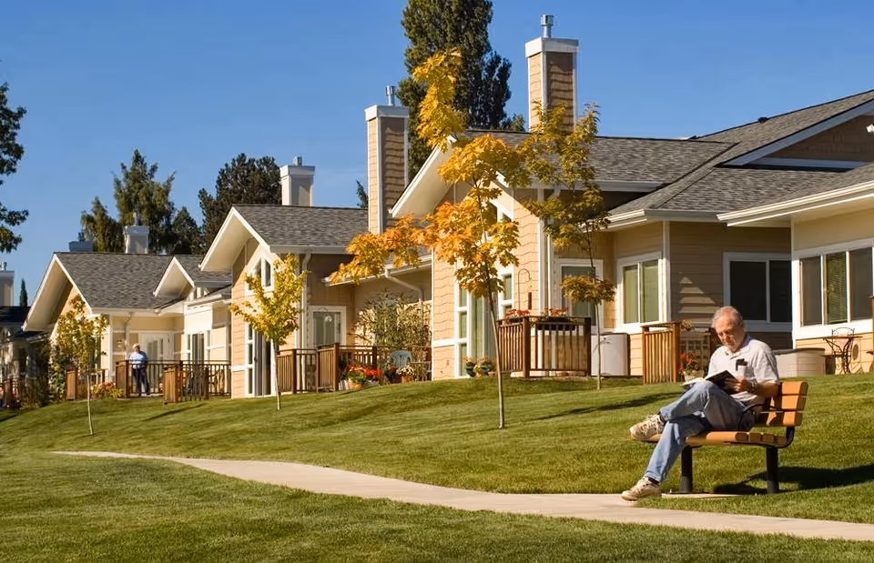 Row of single-story retirement community homes with a green lawn and a man sitting on a bench reading.