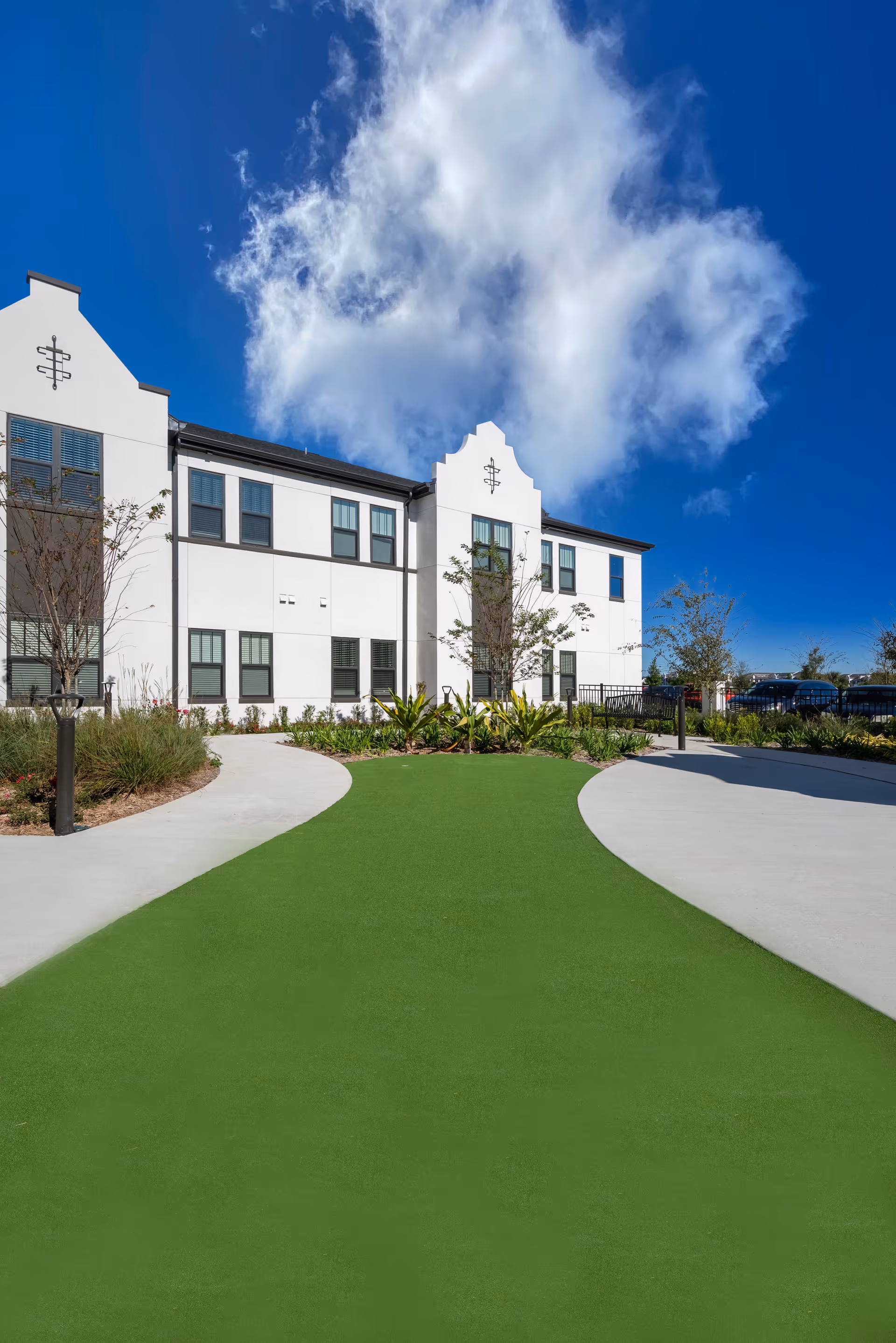 Exterior front view of a white two-story building with a green walkway, landscaped beds, and a bright blue sky with clouds.