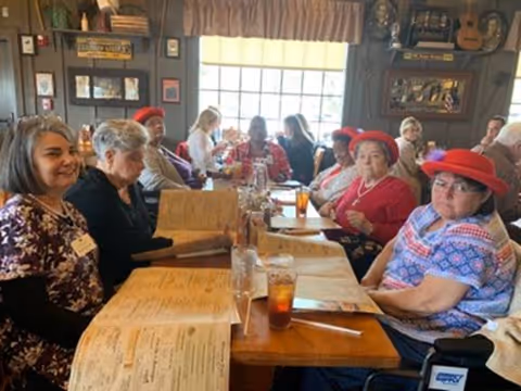 A group of older adults seated around a long dining table indoors, many holding menus and drinks.