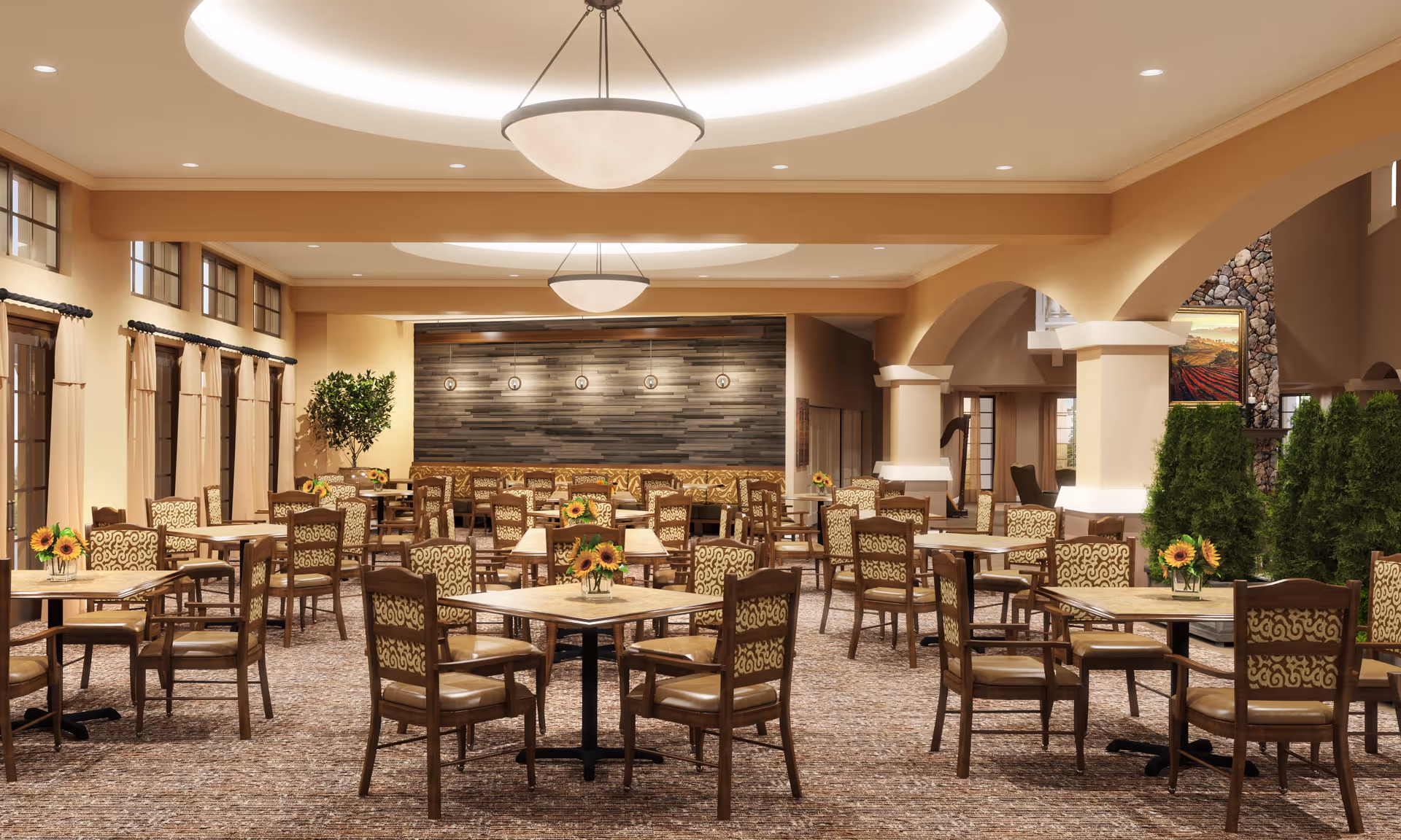 Spacious dining room with multiple wooden tables and chairs arranged neatly. Each table has a small vase with sunflowers. The room features large windows with beige curtains, a patterned carpet, and warm beige walls. There are modern circular ceiling lights and decorative wall lighting on a textured accent wall. Green plants and a stone fireplace with a painting add to the cozy ambiance.