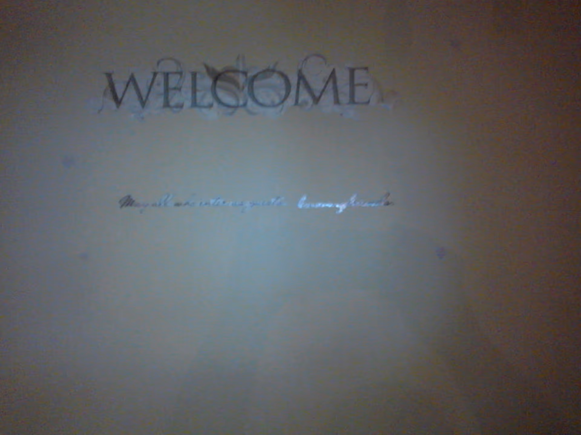 A wall with the word 'WELCOME' written in large decorative letters and a smaller cursive phrase beneath it that is difficult to read.