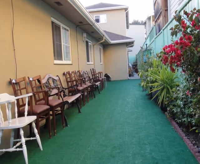 Row of chairs along a beige building on a green outdoor walkway.