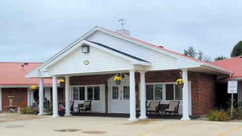 Front view of Anamosa Care Center with a covered entrance, pillars, and outdoor seating.