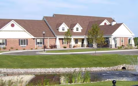 Front view of a senior living facility with brick walls, gable roofs, and a pond.