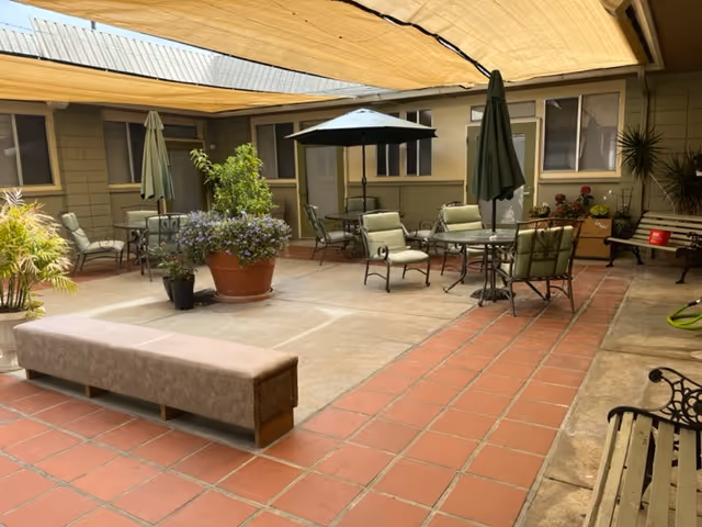 Covered courtyard patio with tables, chairs, umbrellas, potted plants and a bench.
