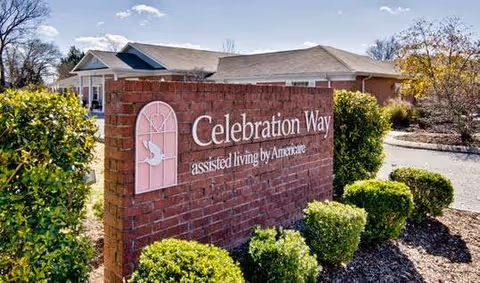 Brick entrance sign reading 'Celebration Way assisted living by Americare' with trimmed shrubs and the facility building in the background.