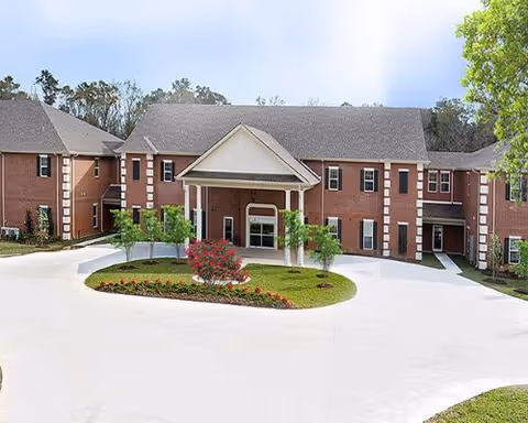 Two-story brick senior living building with circular driveway and landscaped entrance island.