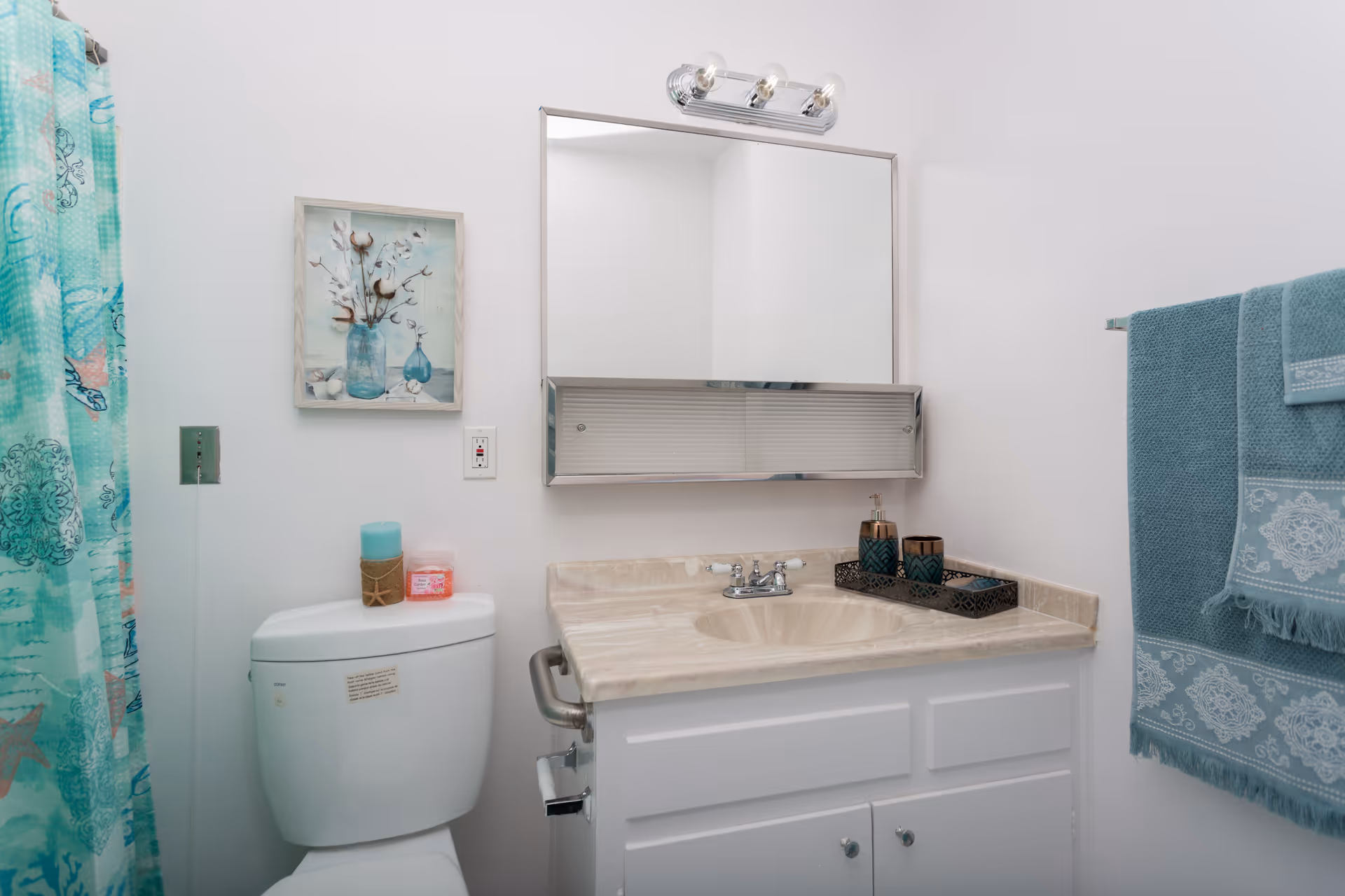 A small bathroom with a sink and vanity, toilet, wall mirror, and teal towels and shower curtain.