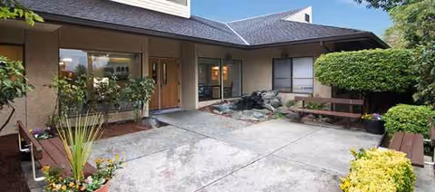 Front entrance to a senior living courtyard with benches, rocks, and potted plants.