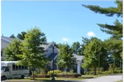 View of a residential building with a light gray exterior surrounded by green trees and bushes under a clear blue sky.