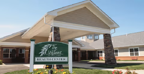 Exterior view of The Willows at Willard Health Center, featuring a covered entrance with stone pillars and a sign.