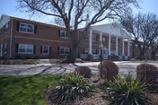 Front exterior of a two-story brick care center with white columns, trees, and landscaped shrubs.