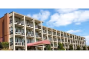 Exterior view of a multi-story brick and concrete building with balconies on each floor under a partly cloudy sky.