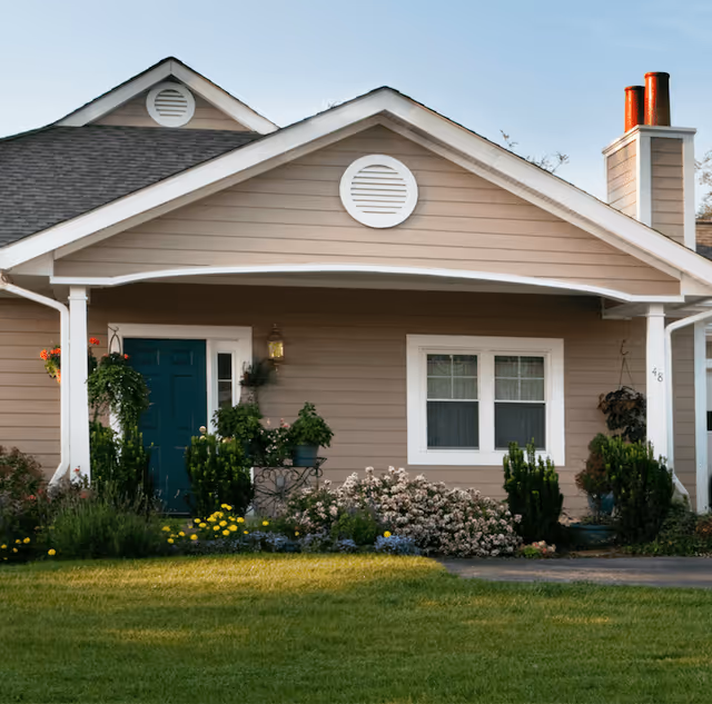Front exterior of a single-story house with a covered porch, teal front door, white-trimmed windows, and a landscaped lawn.