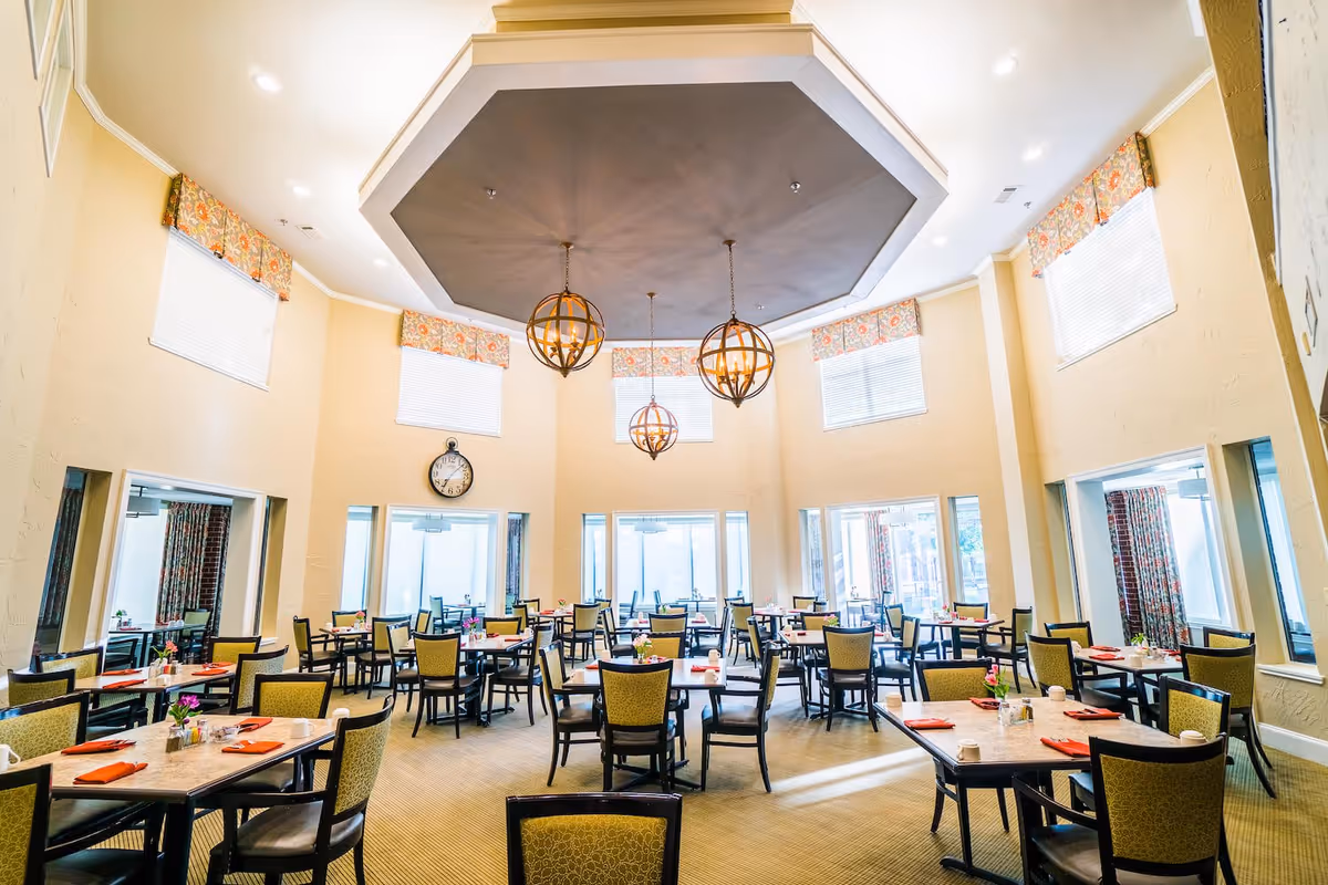 Spacious dining room with multiple set tables and chairs beneath decorative pendant lights and a high coffered ceiling.
