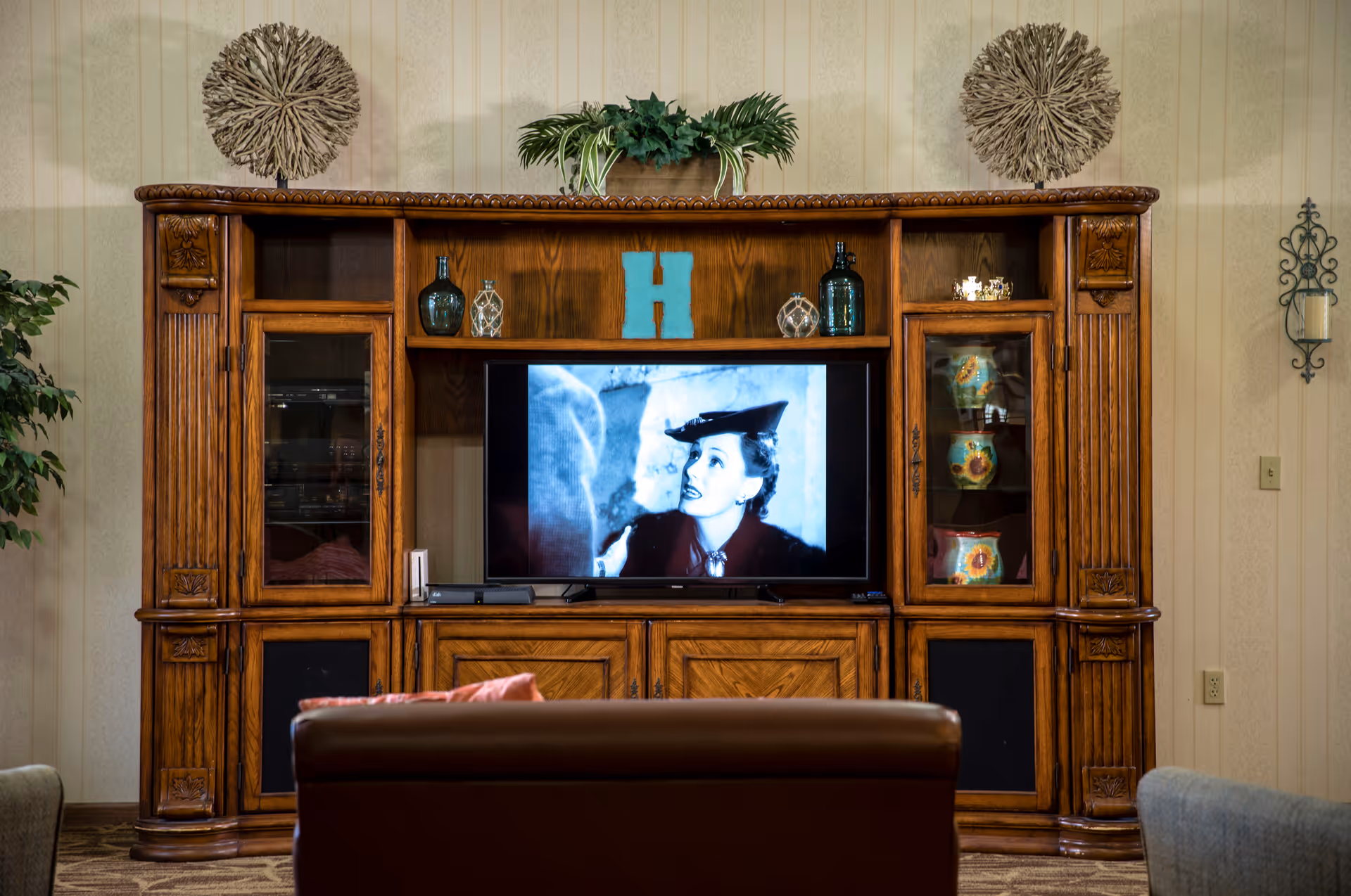 Wooden entertainment center with a TV playing a black-and-white film, decorative objects on shelves, and seating in front in a living room.