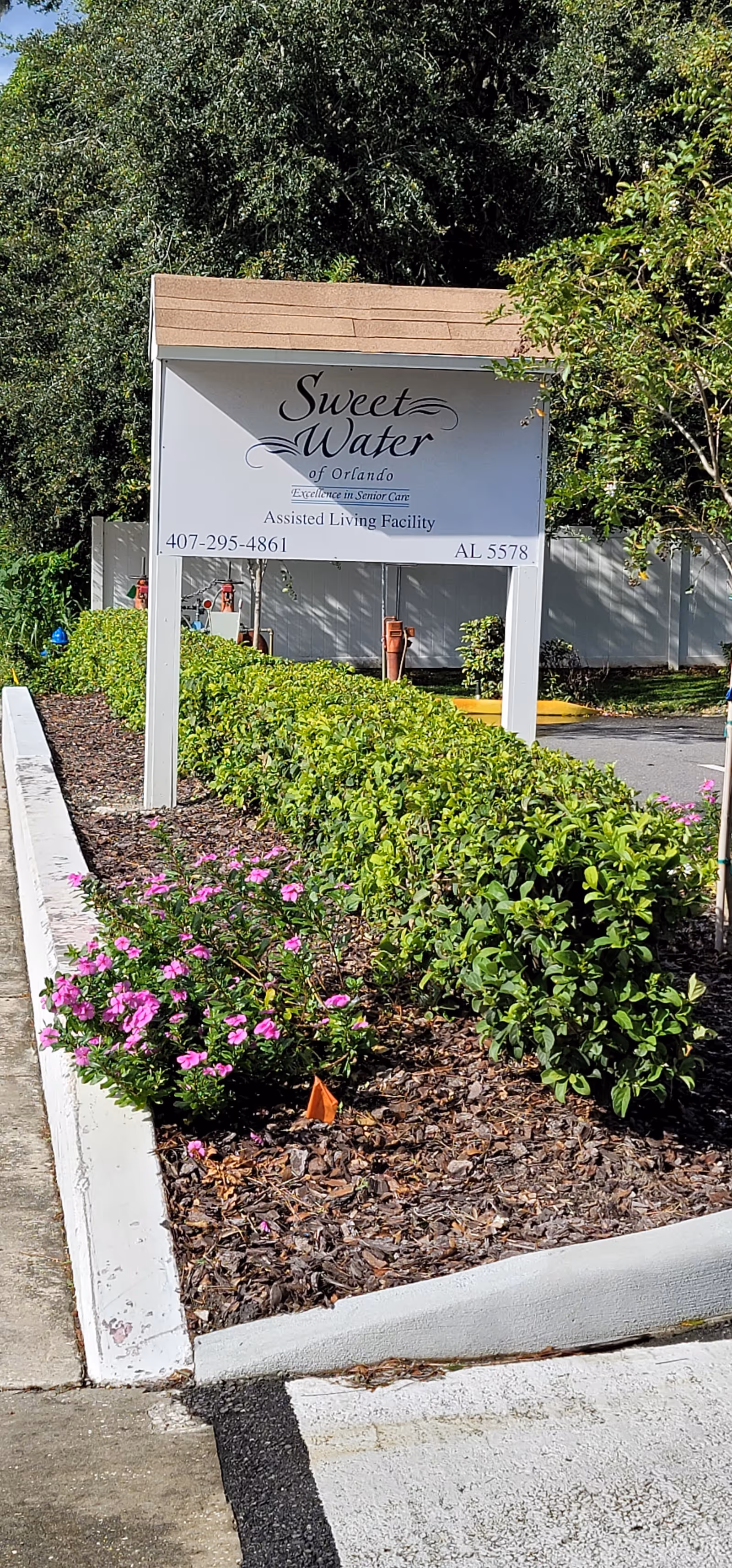 White entrance sign reading 'Sweet Water of Orlando' for an assisted living facility amid landscaped shrubs and pink flowers.