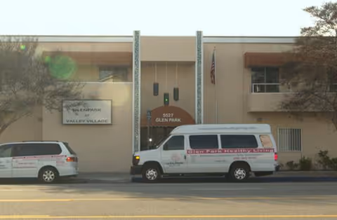 Two parked vehicles flank the entrance of Glen Park at Valley Village senior living facility.