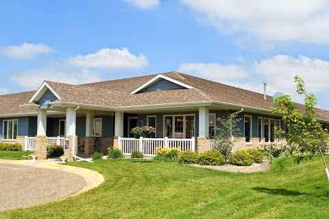 Front exterior of a single-story senior living facility with a porch and manicured lawn.