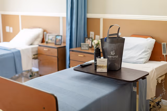 A shared patient bedroom with two hospital-style beds, bedside tables, and a tray holding a Marysville Post-Acute welcome bag and bottle.