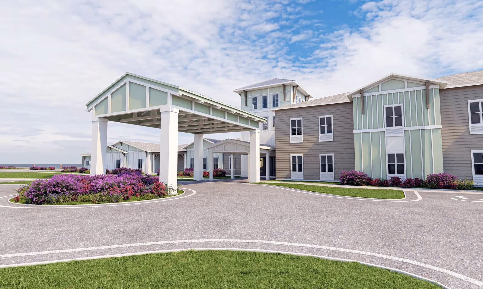 Exterior view of The Canopy at Boynton Ridge facility showing a large covered entrance with white pillars, surrounded by landscaped flower beds with purple and pink flowers. The building has a combination of light green and beige siding with multiple windows and a tower-like structure in the center under a partly cloudy sky.
