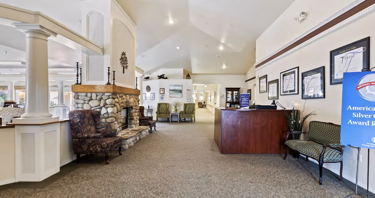 Reception lobby of an assisted living facility with a stone fireplace, seating areas, and a front desk.
