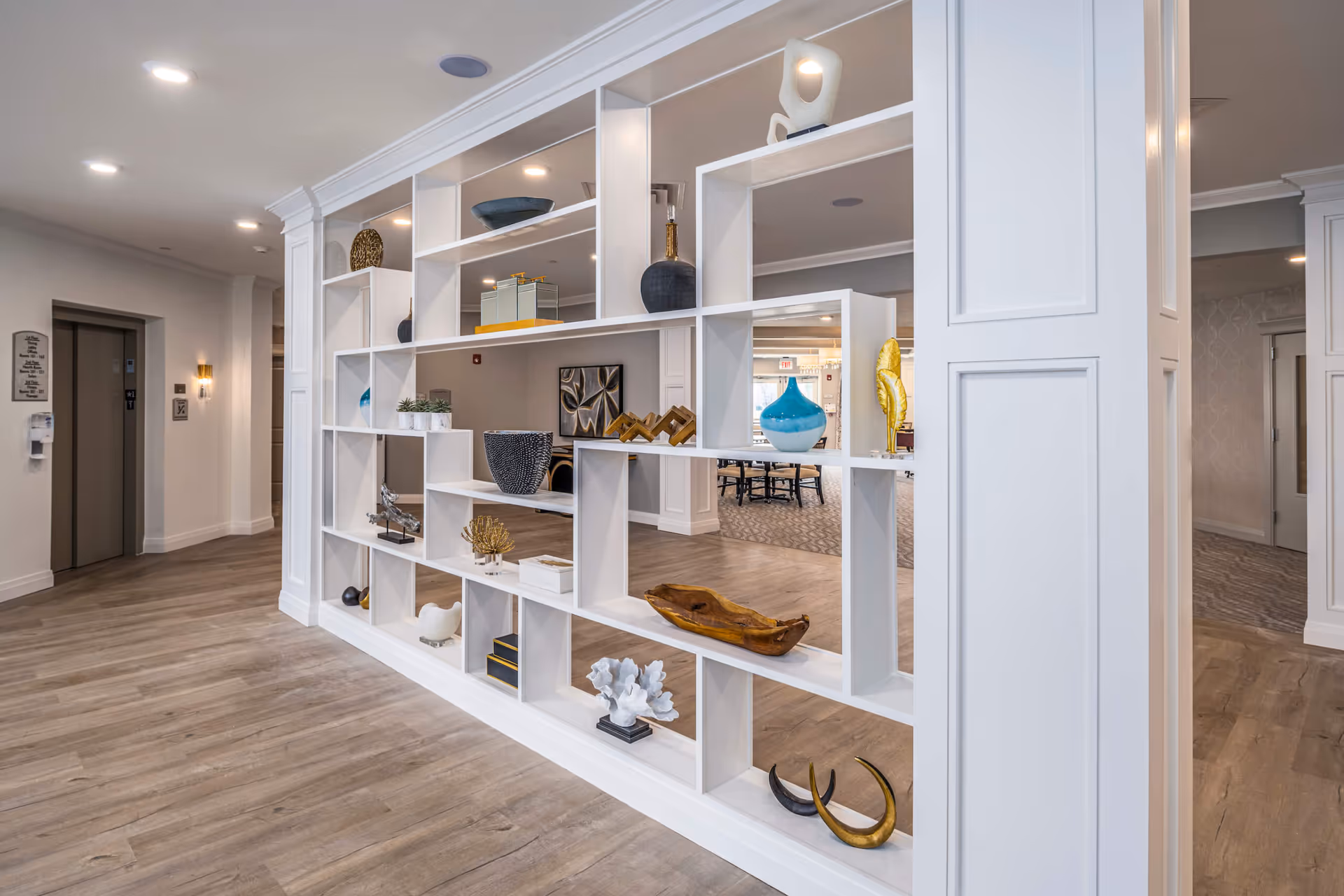 White open shelving partition filled with decorative vases and accents in a bright senior living facility common area.