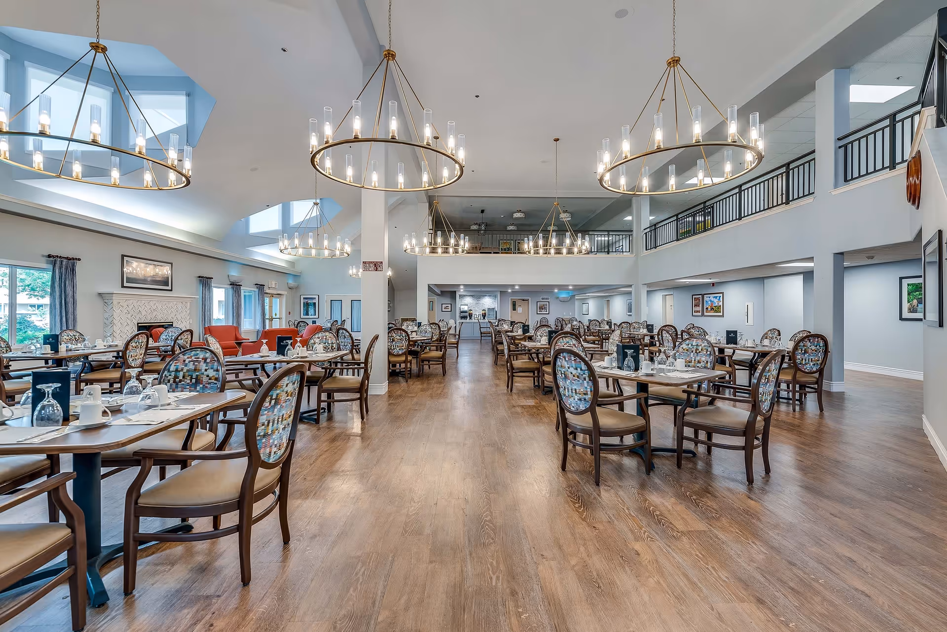 Large, well-lit dining room with multiple tables, chairs, and chandeliers in a senior living facility.