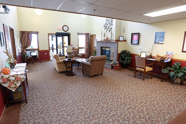 Spacious senior living lounge with chairs and tables arranged around a fireplace and entrance doors.