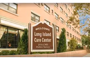 Exterior view of Long Island Care Center building with a sign in front that reads 'WELCOME, Long Island Care Center, 2016 CMS Perfect Survey'. The building is multi-story with several windows and some greenery around the sign.