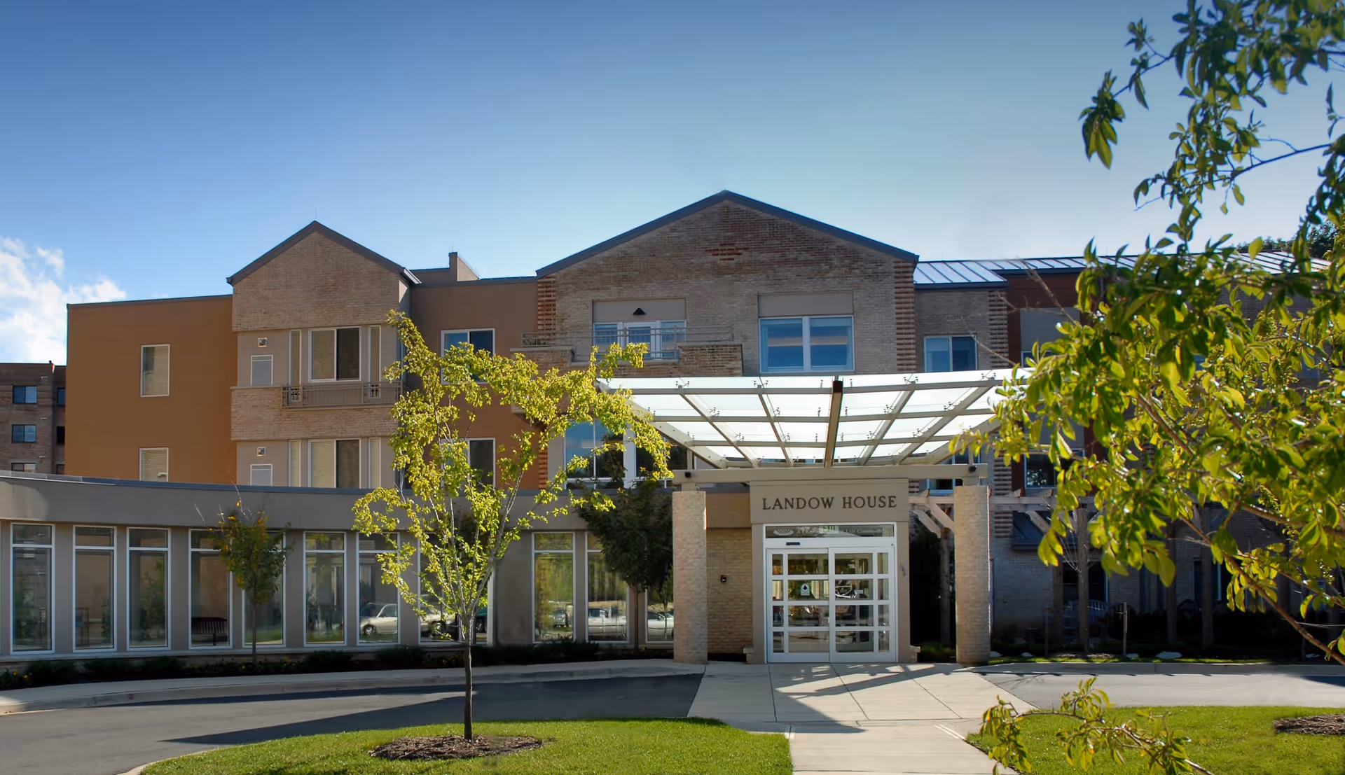 Front exterior view of Landow House, a multi-story building with a glass-covered entrance, surrounded by trees and greenery under a clear blue sky.