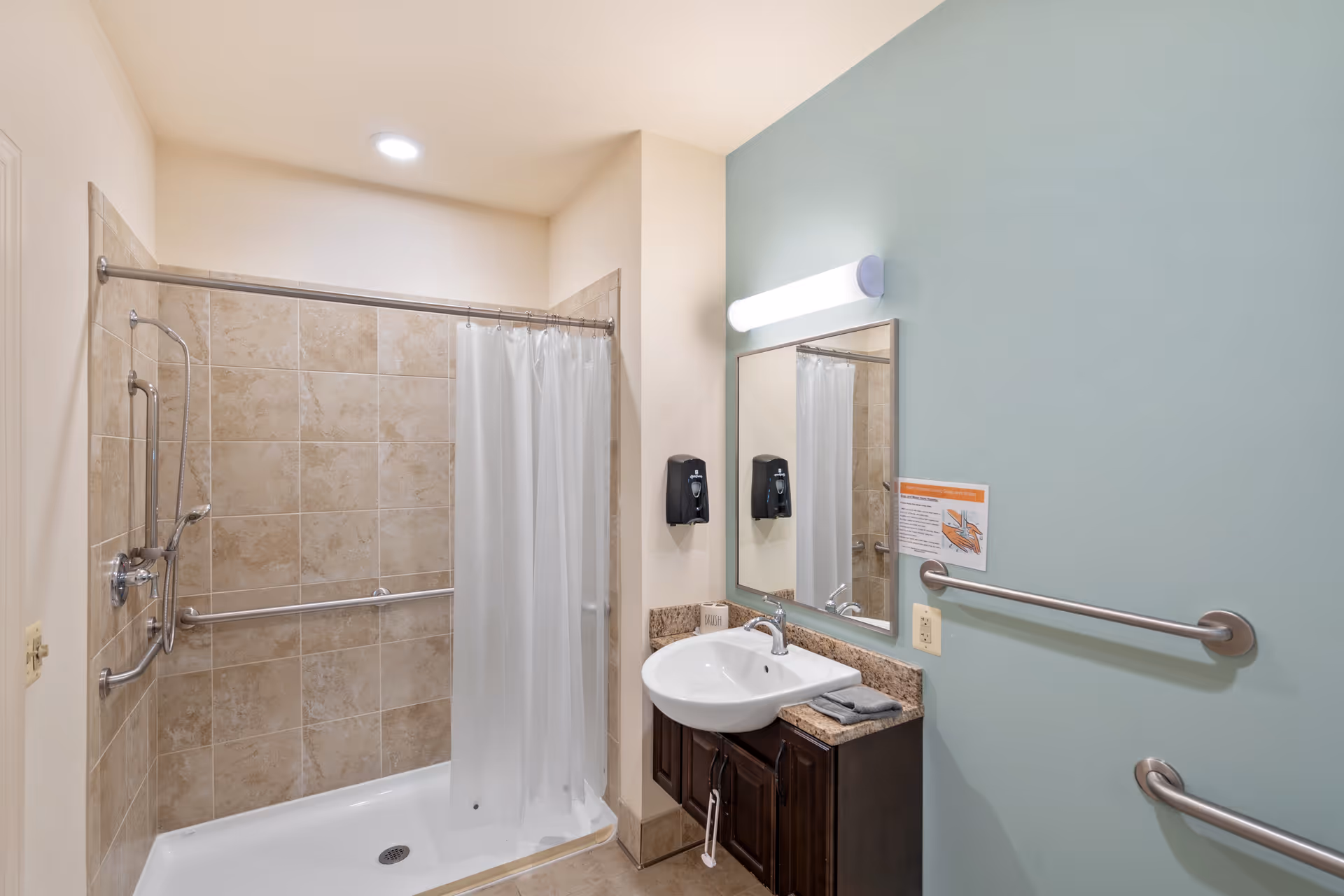 Accessible bathroom with a tiled walk-in shower and curtain, multiple grab bars, a sink with mirror and soap dispensers, and a green accent wall.