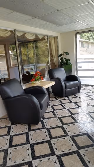 Sunlit sitting area with two black leather armchairs, a small table with flowers, patterned tiled floor, and large windows.