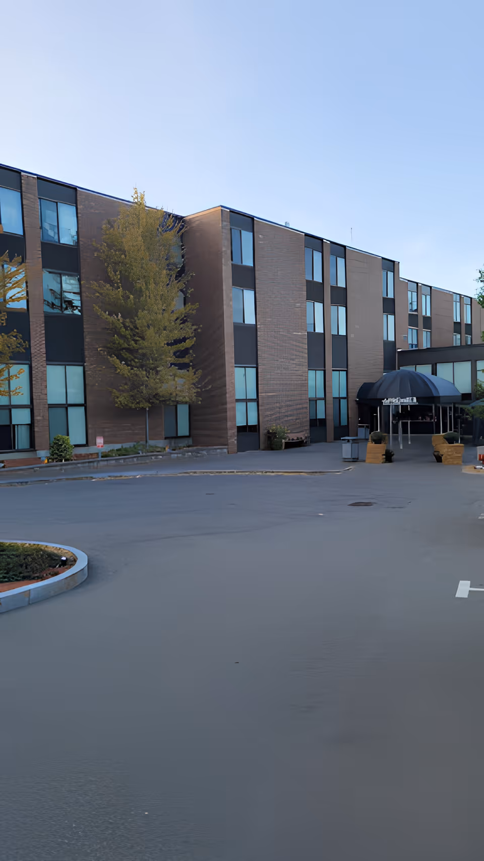 Front entrance and parking lot of a multi-story brick senior care building with a covered drop-off canopy.