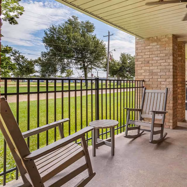 A balcony with two rocking chairs and a small table overlooking a grassy area.