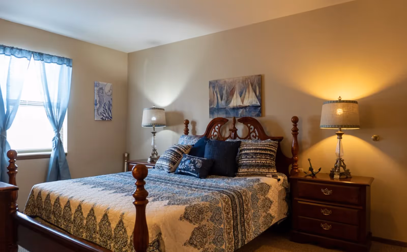 Well-appointed bedroom with a wooden bed, patterned quilt, nightstands and lamps, and a curtained window.