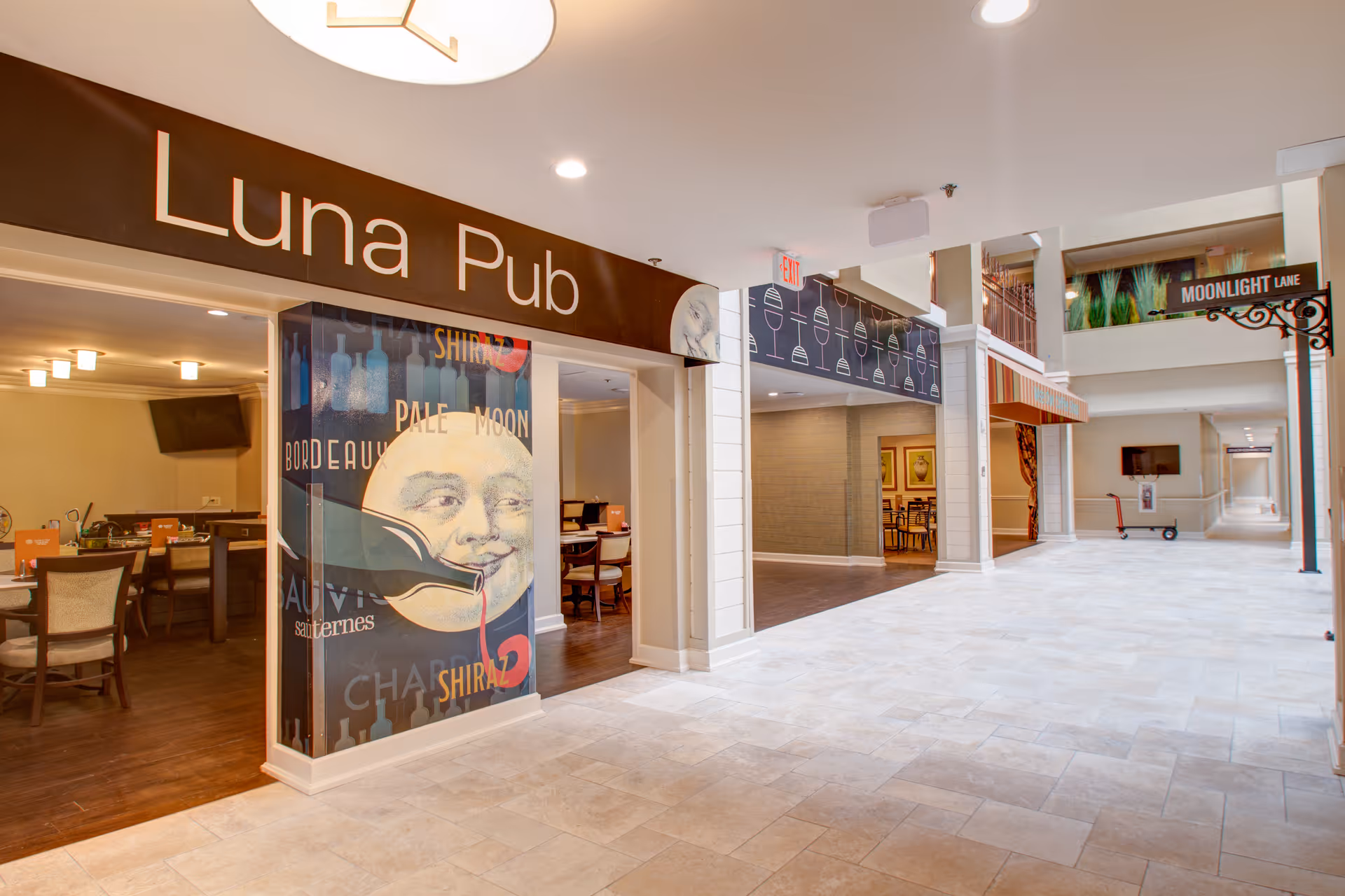 Bright interior corridor of a senior living facility showing the Luna Pub entrance, seating area, and a hallway with a 'Moonlight Lane' sign.