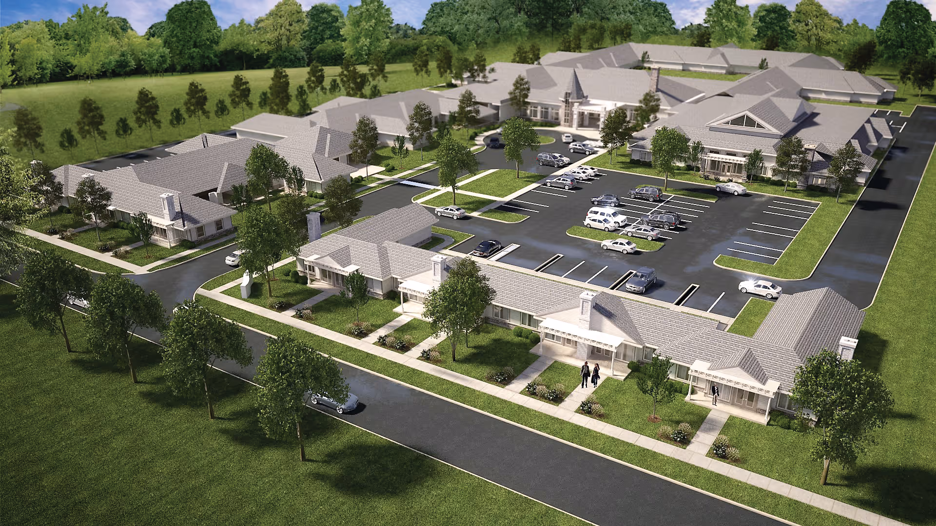 Aerial view of a senior living facility named The Gables of Westerville showing multiple single-story buildings with gray roofs, surrounded by green lawns and trees. There is a parking lot with several cars parked, and sidewalks connecting the buildings. The area is bordered by a road and more greenery in the background.